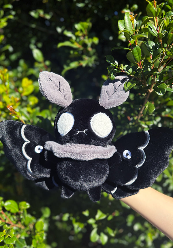 Black plush toy with white accents held against a green leafy background