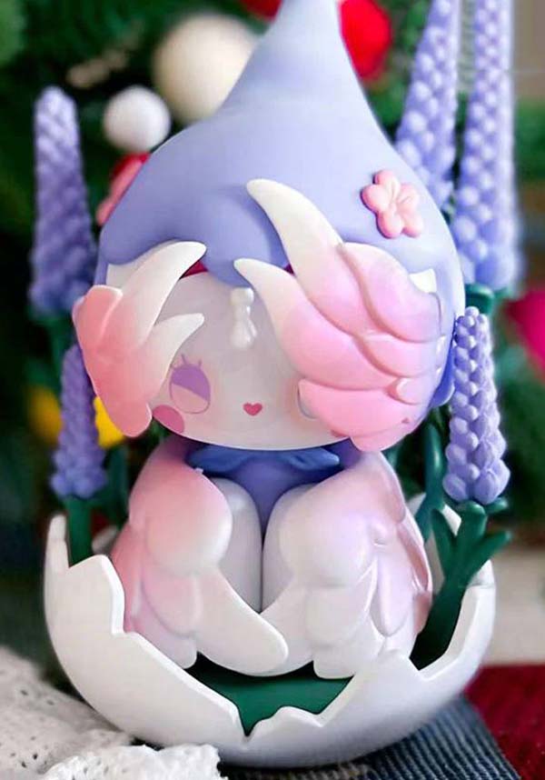 Cute character figurine with pastel colors in an egg, surrounded by flowers.