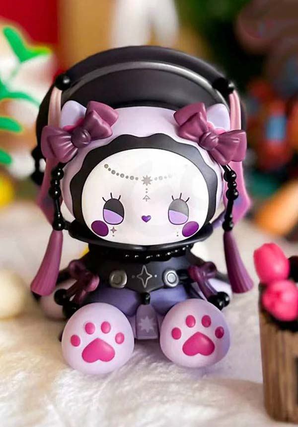 Cute figurine with purple bows and pink paw prints on a soft surface.