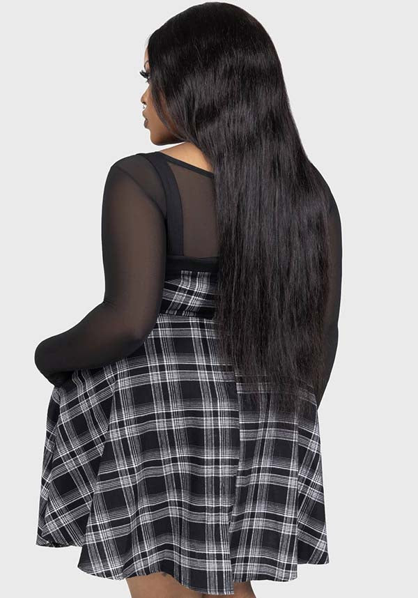 Person wearing a black and white plaid dress with sheer sleeves on a light gray background