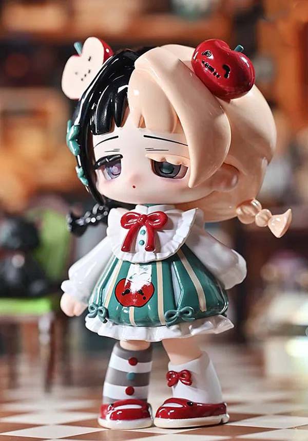 Toy figure with black hair, red bow, and green and white outfit on a checkered floor.
