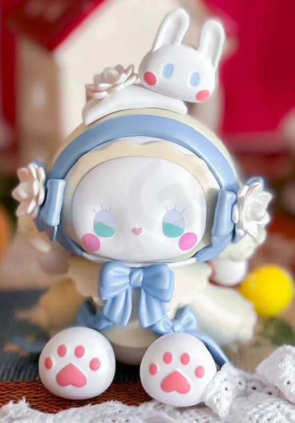 Cute cartoon character figurine with bunny ears and bow tie on a textured surface.