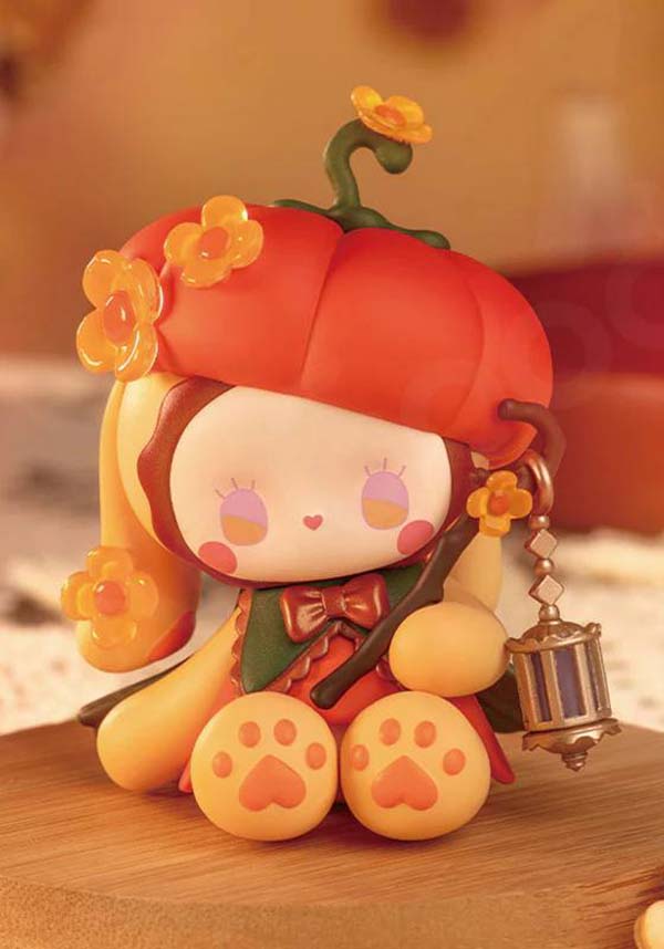 Toy figure of a character in a pumpkin costume with a lantern on a wooden surface.