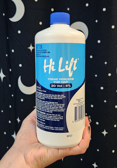Hand holding a bottle of Hi Lift cream peroxide against a star-patterned curtain background