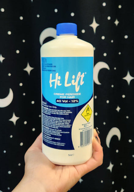 Hand holding a bottle of Hi Lift hair product against a black curtain with white patterns
