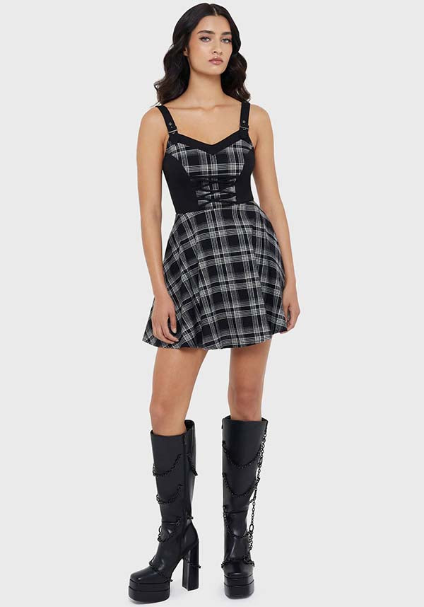 Woman wearing a black and white checkered dress with knee-high black boots on a white background